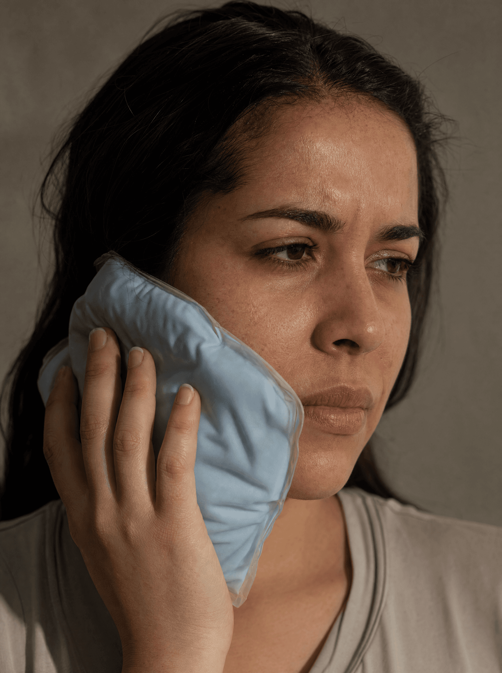 Close-up of a person holding a cold pack to their cheek, concerned expression